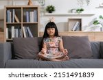 Small photo of Calm of Asian child cute making yoga meditation with inhale and exhale. Sit on couch for focusing mind and soul. Relaxed with hand pleat in living room, indoor meditating for peaceful with yoga.