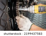 Motorcycle mechanic wearing gloves using impact wrench and Drive Socket working repair back sprocket of  motorcycle at motorbike garage ,motorcycle maintenance and repair concept,
