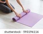 Young yoga Woman rolling her lilac mat after a yoga class on wooden floor near a window, close up