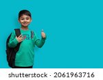Small photo of Happy smiling boy with thumb up is going to school. Child with school bag and books. Kid indoors on a background. Back to school.