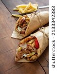 Small photo of Gyro Shawarma pita bread on wooden table. Greek food, sliced meat, potato, tomato and tzatziki, paper wrap, copy space.