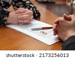 Small photo of Signing a divorce, marriage dissolution documents and agreement. Wife and husband hands, wedding rings and legal papers for signature on a wooden table, lawyer office