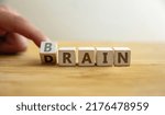 Small photo of Brain drain concept. Finger flips letter at wooden cube changing the word brain to drain. Message about emigration, the departure of educated and professional people from their country.