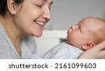 Small photo of Happy mother babbles with newborn baby girl holding in arms on blurred background. Woman kisses face of cute little well-fed daughter at home, closeup