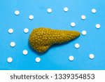 Small photo of 3D anatomical model of pancreas gland is on blue background surrounded by white pills as ornament polka dots. Medical concept by pharmacological tableted treating of pancreas disease, pharmacotherapy