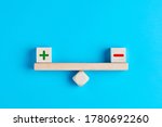 Plus and minus or positive and negative symbols on wooden blocks are in balance on a wooden seesaw. Blue background, flat lay view. Pros and cons equilibrium in decision making under uncertainity. 