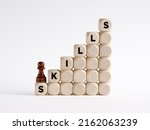 To develop personal, social or technical skills concept. Chess pawn is climbing the ladder of wooden cubes with the word skills.