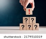 Small photo of Concept of uncertainty, confusion and suspicion. Hand puts a wooden cube with exclamation mark at the top of stacked cubes with question mark.