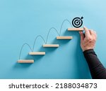 Male hand arranges a wooden block staircase with target icon. Achieving goals and objectives or goal setting concept.
