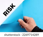To uncover hidden business risks concept. Male hand opens the blue paper and reveals the word risk.