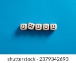 Small photo of Unhappy member of the team. Teamwork adaptation. Work stress. Social nonconformity. One unhappy face between happy faces on wooden cubes.