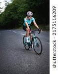 Small photo of Professional female cyclist trains in the woods. Woman riding race bicycle on a forest asphalt road, uphill, front view
