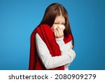 Young kid feels unwell, blows nose in white tissue, suffers from running nose, cold symptoms or allergy, sneezes very often, wearing red scarf