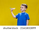 Little boy in a blue T-shirt holds a toy white plane and plays on a yellow background. Copy space. Travel concept.