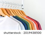 close up a collection of pastel color t-shirts hanging on a wooden clothes hanger in closet or clothing rack over white background, copy space