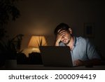 tired male businessman works at home at night on a laptop, works from a home office, studies online,. Internet addiction or a person who works late. a frightened man works late at his home office