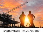 Small photo of A team of engineers on a construction site pass a blurry construction site at sunset.