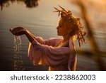 Small photo of A beautiful woman in a white dress with a wreath on her head stands in the water. Slavic girl bathes in the lake at sunset. Ivana Kupala