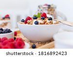 bowl of fresh oat flakes müsli with raspberry and blueberry standing on the breakfast table with fresh milk and a cereals jar in blurry background. summer fitness diet concept.