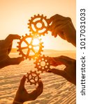 Small photo of four people hold gears on sunset background. concept of teamwork. coherence in work