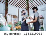 young couple florist wearing apron and face mask holding bucket flower smiling helping each other working in flower shop following protocol healthy