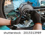 male bicycle mechanic's hand in gloves attaches chain over rear derailleur and sprocket in workshop