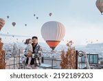 Small photo of happy family looking at hot air balloon flying around them when visiting cappadocia turkey in winter