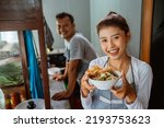 Small photo of female waitress smiling while bringing a bowl of chicken noodles for customers in a stall cart