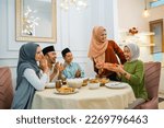 Small photo of group of Muslims celebrating and giving gifts to veiled woman while gathering at a dinner table