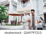 Small photo of Asian Muslim husband and wife smiling intimately with hands holding in front of the house