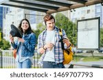 Two students while waiting transport on bus or tram stop for going to university using mobile phones and paying no attention to one another. Phone addict youth, modern lifestyle concept