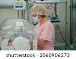 At the intensive care unit. Nurse standing near hospital bed with a baby preparing it for treatment. Newborn is placed in the incubator. Neonatal intensive care unit