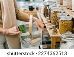 Close up shot of woman carrying shopping basket and shopping groceries zero waste shop with glass jars on shelves..