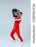 Small photo of cheerful fashionable man wearing a red sports suit dancing jumps with a retro tape recorder. interesting and fervent style of the 90s.