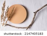Small photo of Empty round beige platform podium, dry tree twigs and bent grass on white linen fabric background. Minimal creative composition background for cosmetics or products presentation. Top view