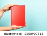 Small photo of Woman hands holding book with blank red cover over light blue background. Education, back to school, self-learning, book swap, sharing, bookcrossing concept