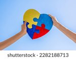 Small photo of World autism awareness day, Autism spectrum disorder concept. Adult and child hands holding together colorful painted puzzle heart on blue sky background.