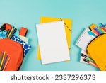 Back to school, education, learning concept. Two open backpacks with school supplies and open white spiral sketchbook notebook on pastel green background. Top view