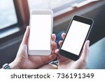 Mockup image of a woman's hands holding two mobile phones with blank white screen in modern cafe