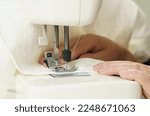 Work at home. Small business. A female seamstress sews white fabric items on a sewing machine. Close-up.