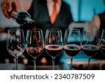 Party and celebration concepts. Bartender pours red wine in glasses at bar. Male sommelier pouring red wine into long-stemmed wineglasses.