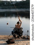 Small photo of The fisherman sits on the bank of the river in a chair. The fisherman casts his bait into the river. Feeder with bait and bait.