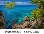 Beautiful turquoise and blue water near rocks and cliffs in Negril, Jamaica. A tree on the left and rocks on the right with a beautiful lagoon in the sea