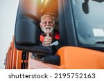 Senior garbage removal worker driving a waste truck. He is showing thumb up.