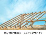 Wooden rafters against the blue sky in house under construction. Installation of rafters on the roof of a house under construction against the background of the sky
