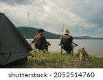 Friendship fisherman or Angler sitting a chair together and camping to fishing at the lake. Camping tent on the shore of the lake. Survival concept.