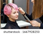 Hairdresser checks short pink hairstyle of young woman in hair salon.