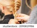 Small photo of Braiding braid. Hands of female hairdresser braids long braid for a blonde woman in a hair salon
