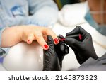 Small photo of Manicure varnish painting. Close-up of a manicure master wearing rubber black gloves applying red varnish on a female fingernail in the beauty salon