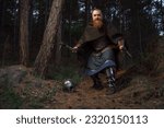 Small photo of Medieval red-haired viking warrior with beard with two axes is preparing to attack on forest path.